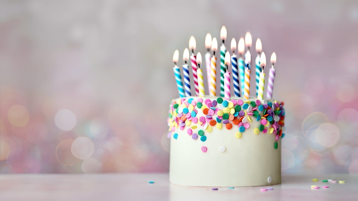 Colorful celebration birthday cake with sugar sprinkles and birthday candles against fairy lights