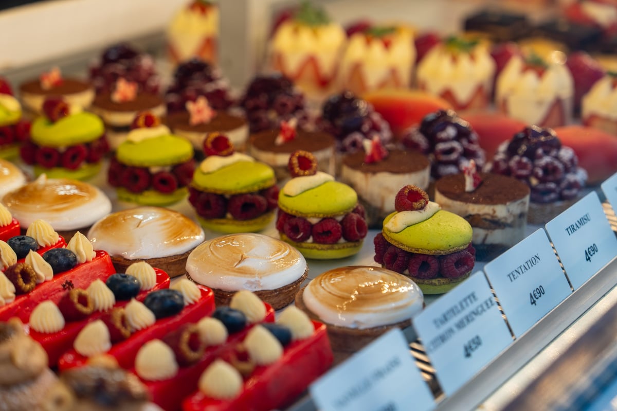 A wide variety of pastries showcased behind a glass display in a cozy bakery with vibrant mini cakes, macarons, and fruit tarts