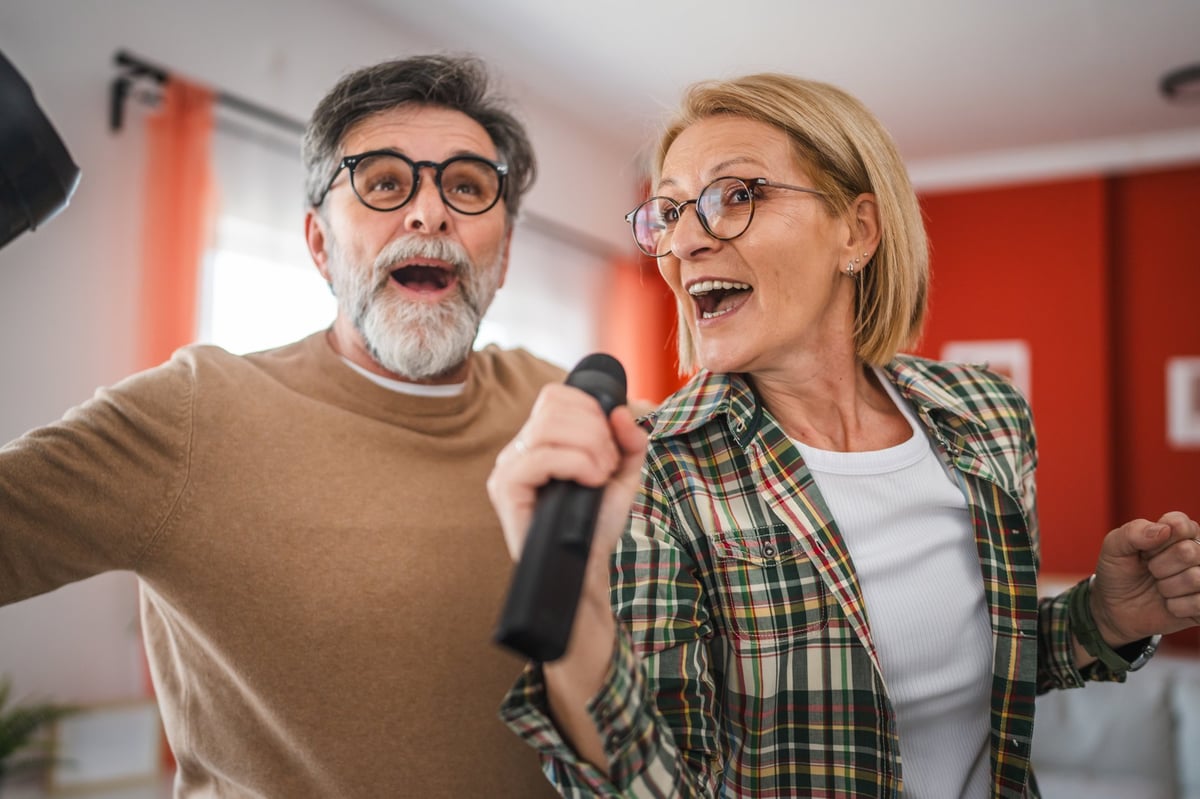 Mature couple husband and wife singing dancing karaoke party at home