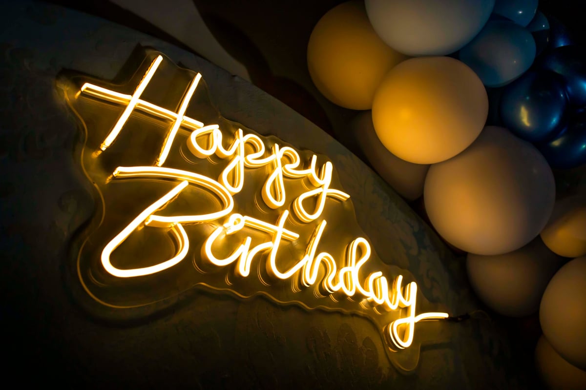 Glowing neon happy birthday sign with colorful balloons creating a vibrant party atmosphere