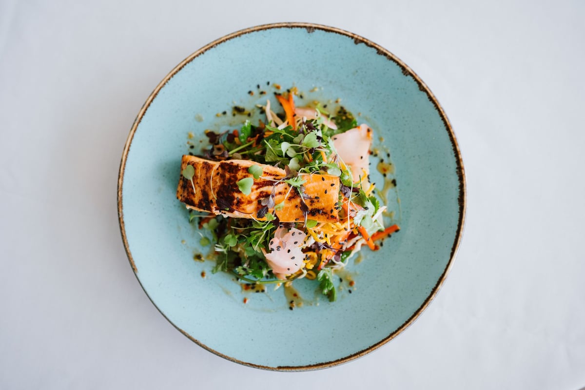 A gourmet dish of grilled salmon with fresh greens and vegetables served on a blue plate