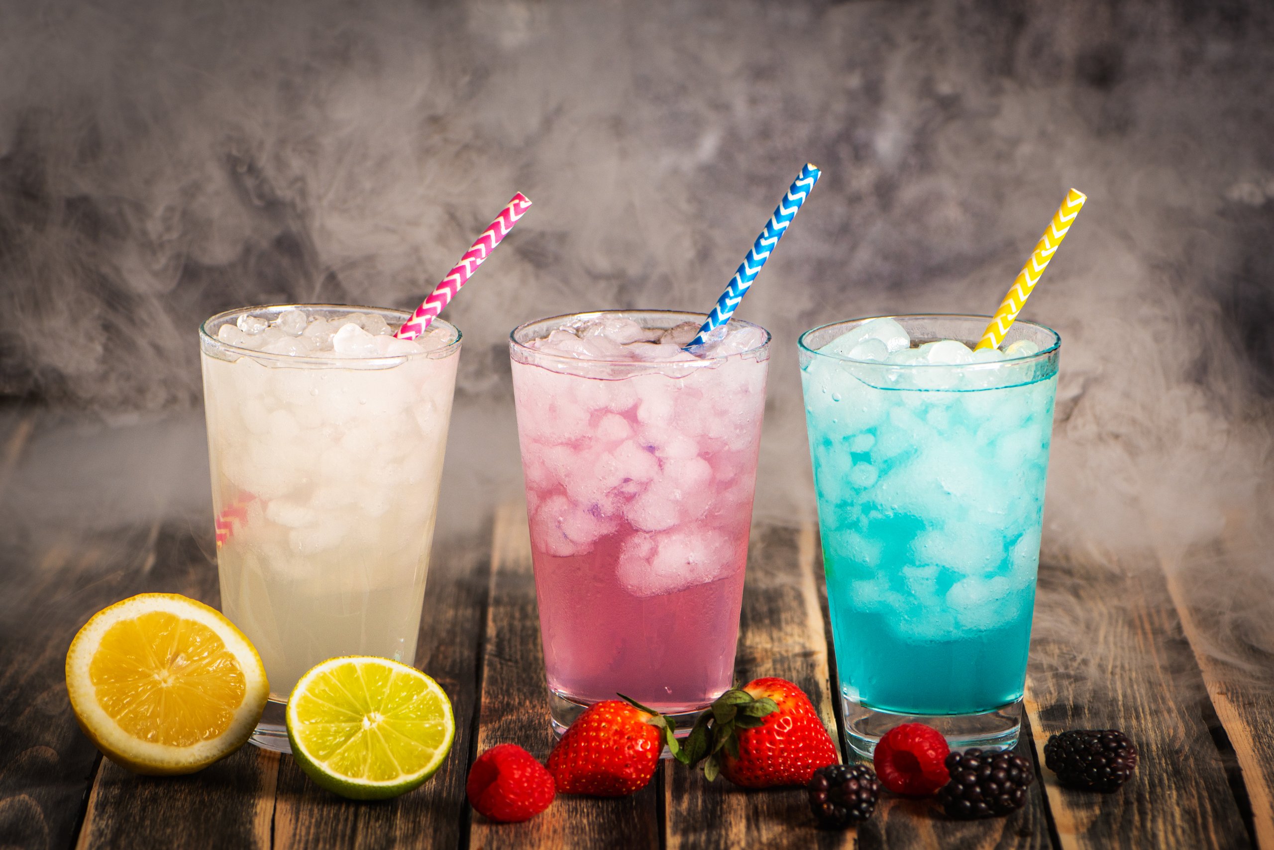 Glasses with ice surrounded by smoke, filled with colorful soft drinks of various flavors