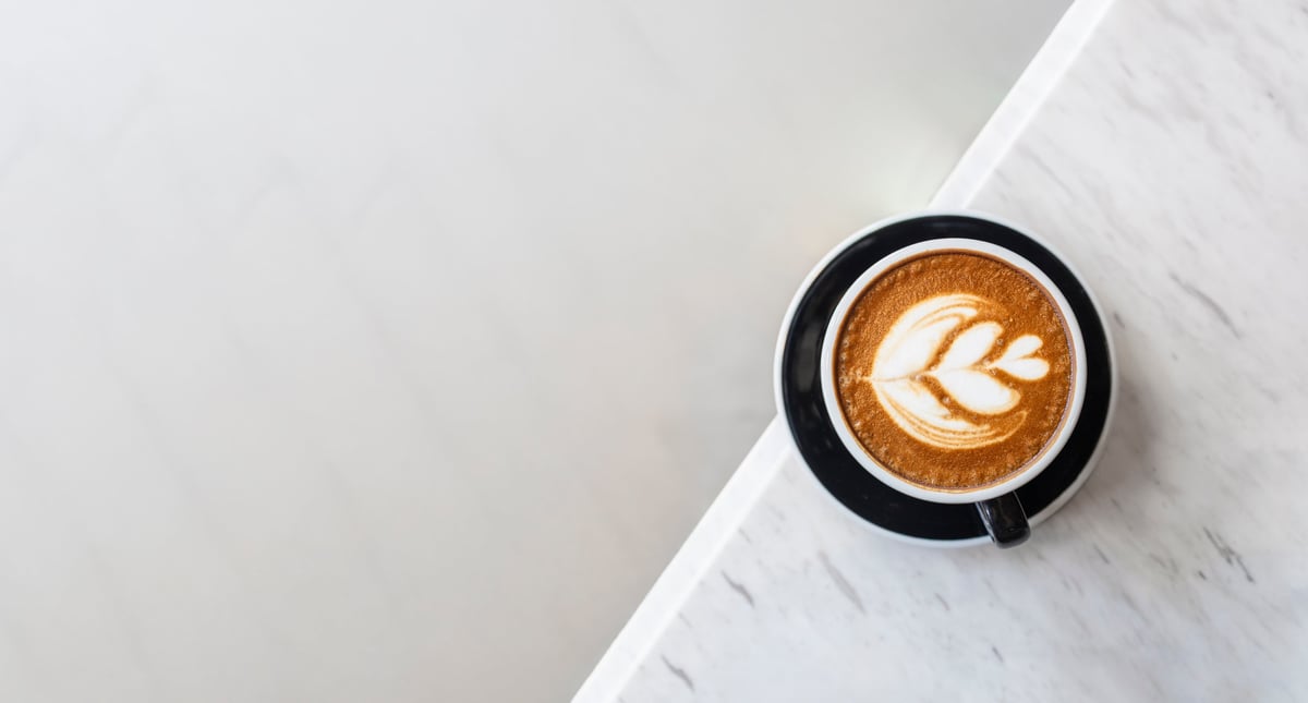 Overhead shot of latte art in black coffee cup on white marble table, minimal and elegant cafe concept