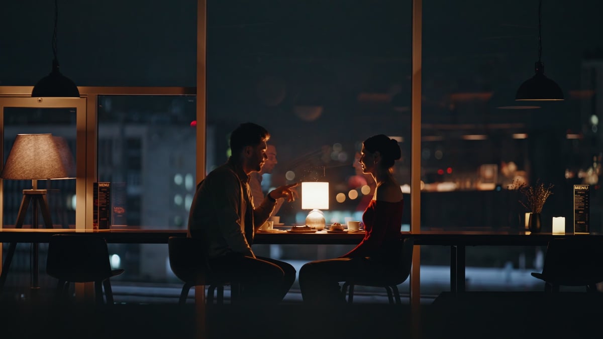 Happy couple sitting by panoramic window with city view enjoying romantic evening date