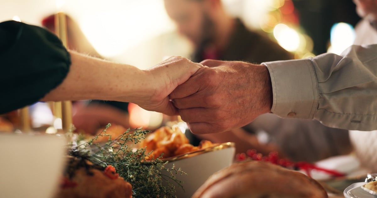 Holding hands Christmas prayer with family at dinner table for gratitude holiday season