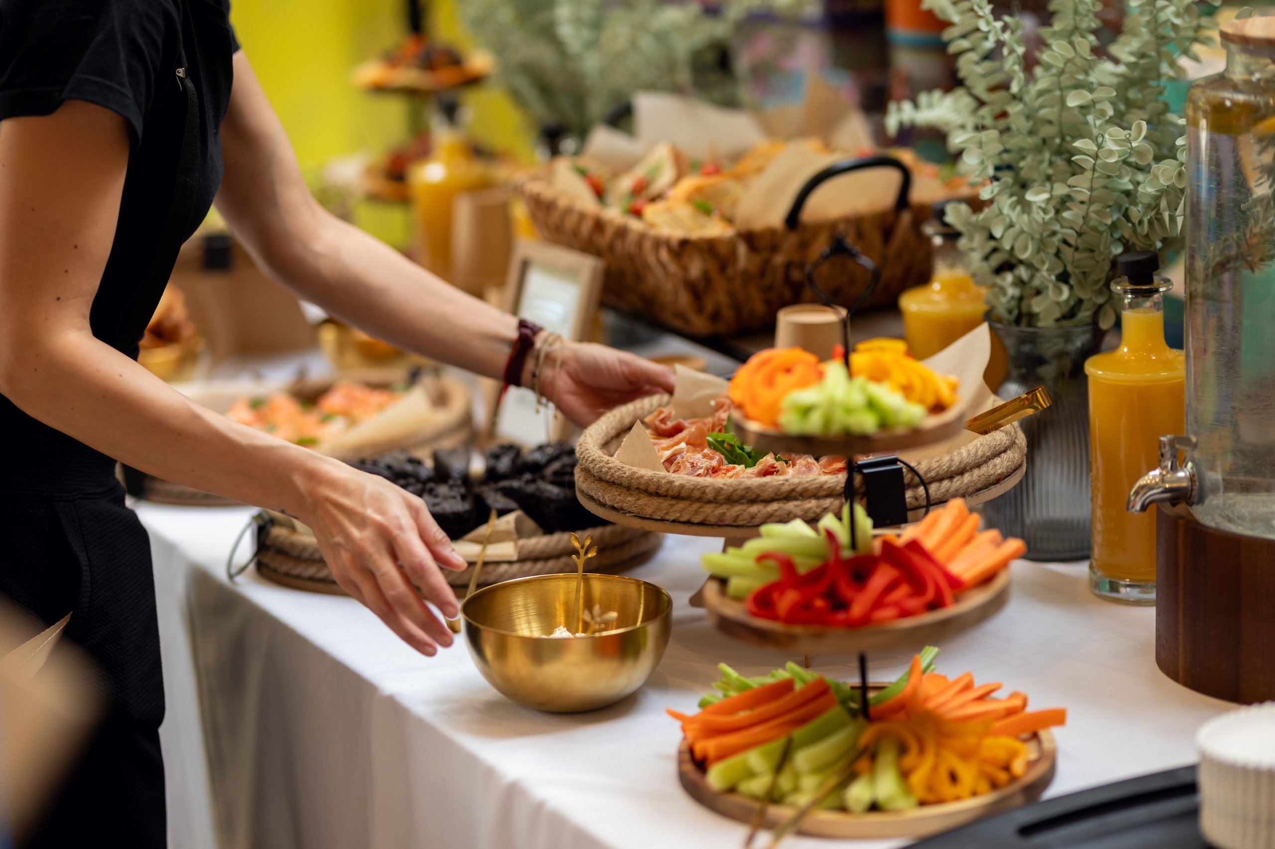 Professional caterer arranging buffet with colorful sandwiches, fresh vegetables, and tempting desserts