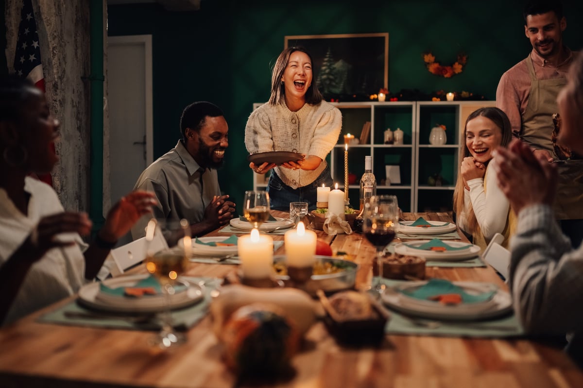 Happy multi-ethnic friends and family laughing enjoying festive meal together at home