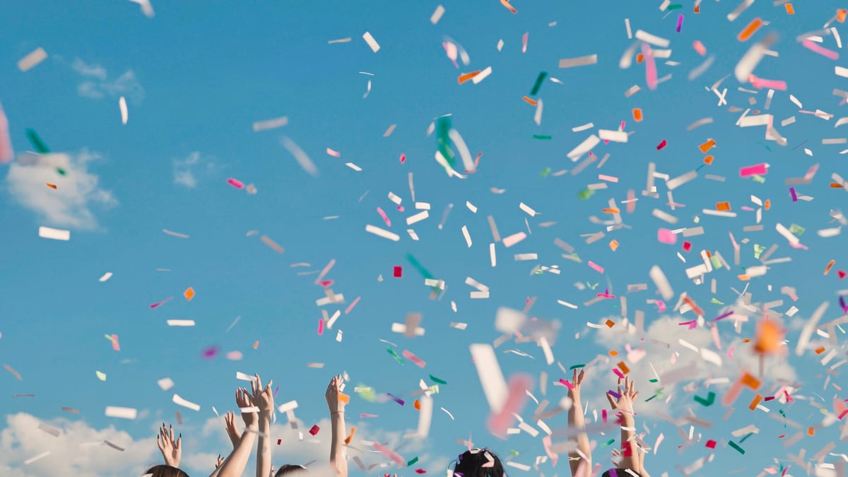 Group of cheerful high school students throwing colorful confetti celebrating graduation under blue sky
