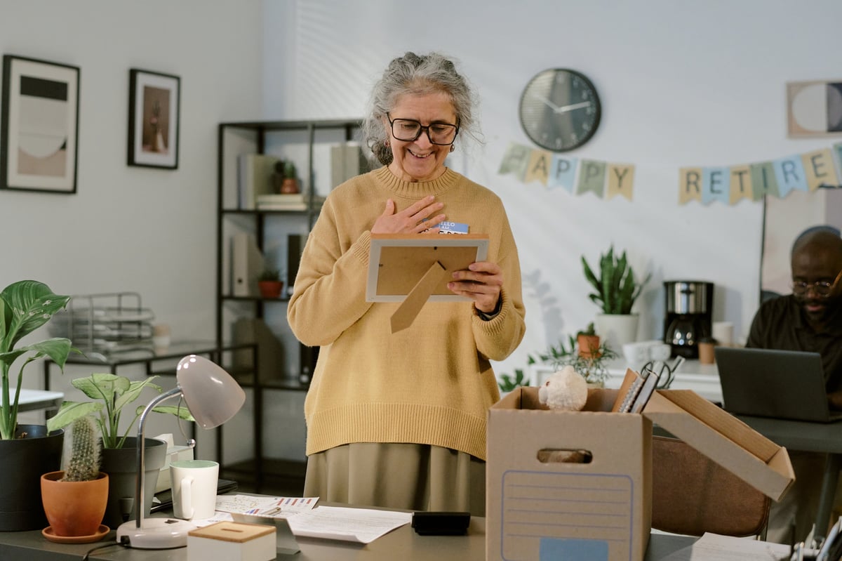 Senior woman standing in office holding picture frame smiling during retirement celebration
