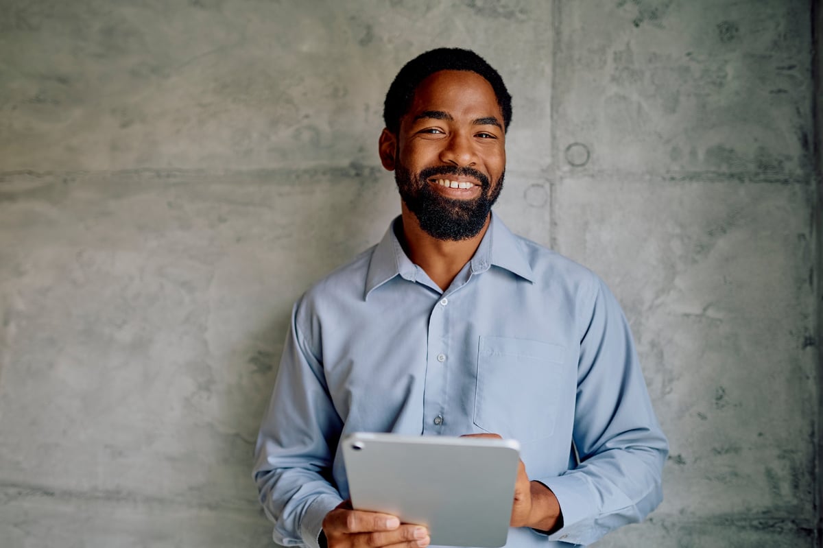 Businessman smiling at camera holding a digital tablet, corporate portrait
