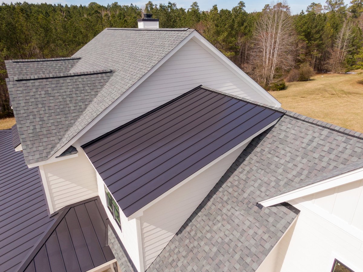 Drone aerial image of a custom residential home under construction featuring a combination of asphalt shingles and standing seam metal roofing