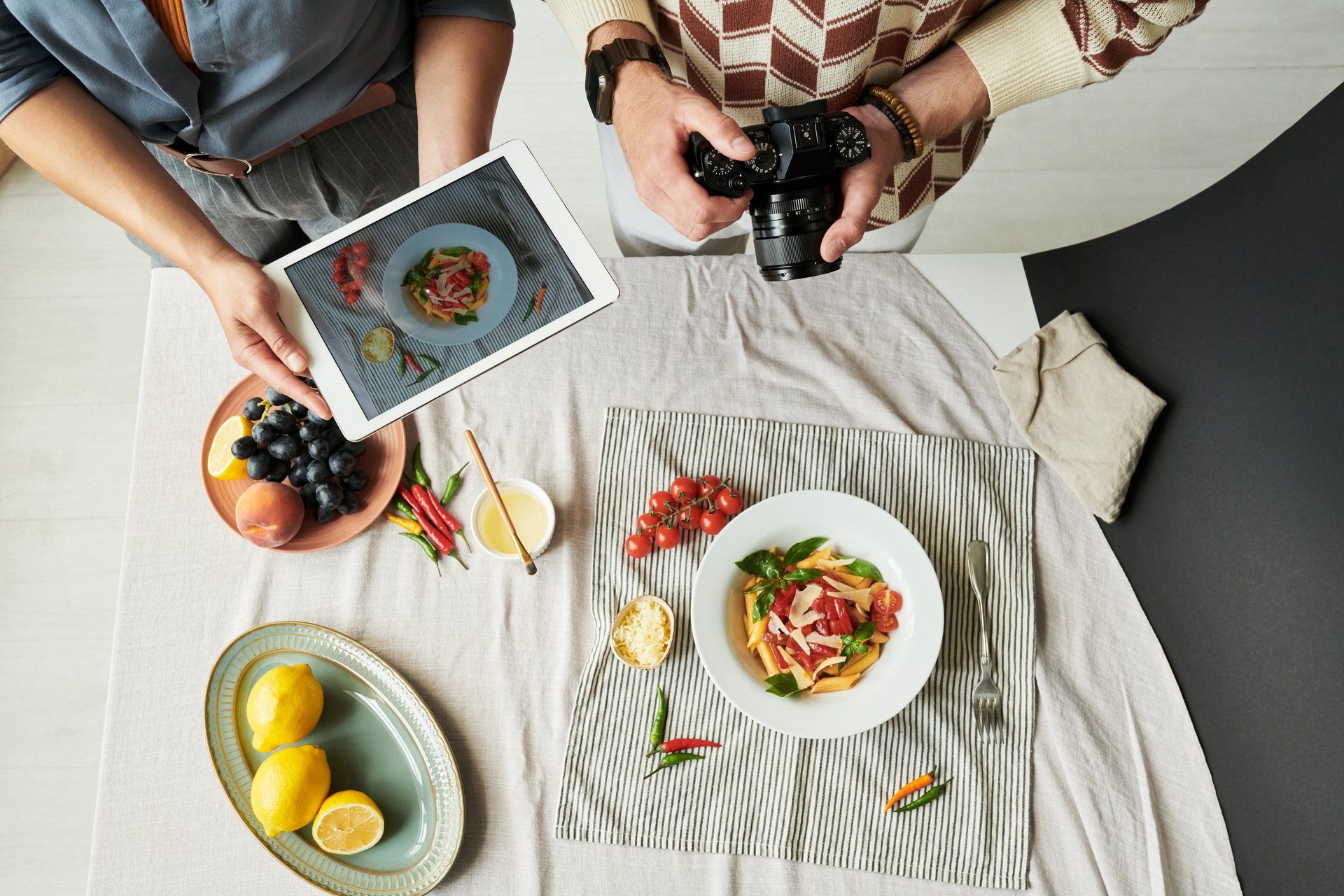 Woman holding tablet photographing salad while man using camera capturing food on table