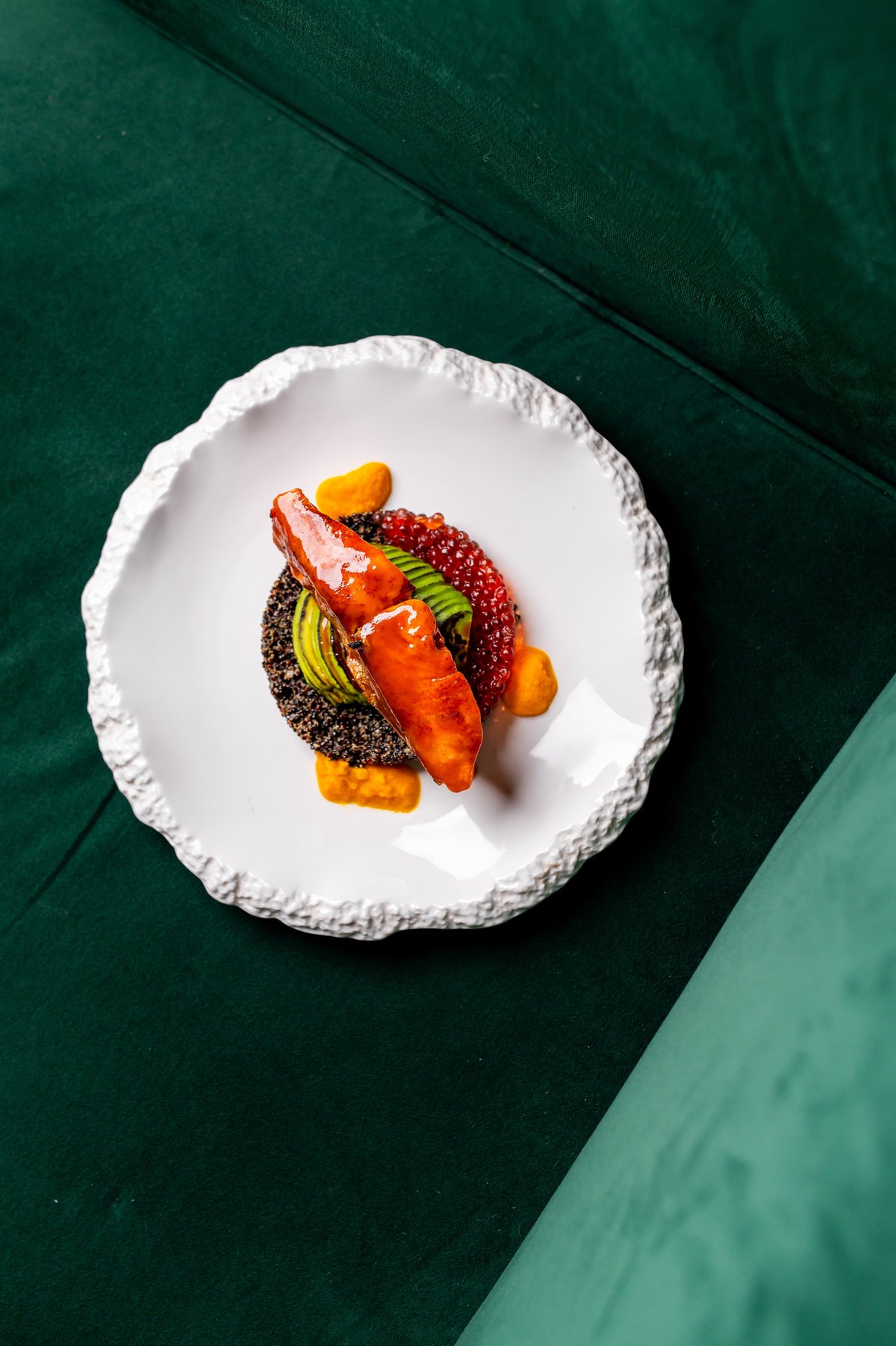 Gourmet dish with plated salmon, red caviar, avocado, and sauce on a modern white plate