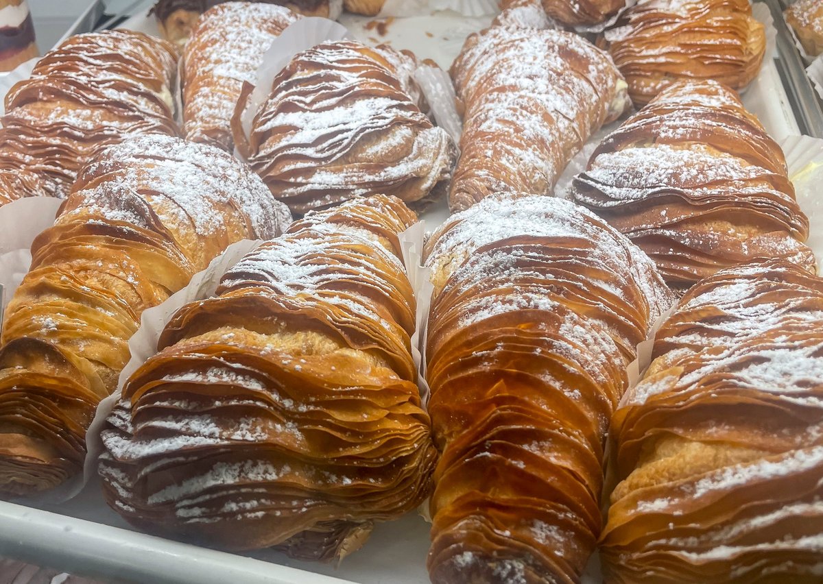 Flaky, golden sfogliatelle pastries stacked in a bakery display, their crisp layered shells dusted with powdered sugar
