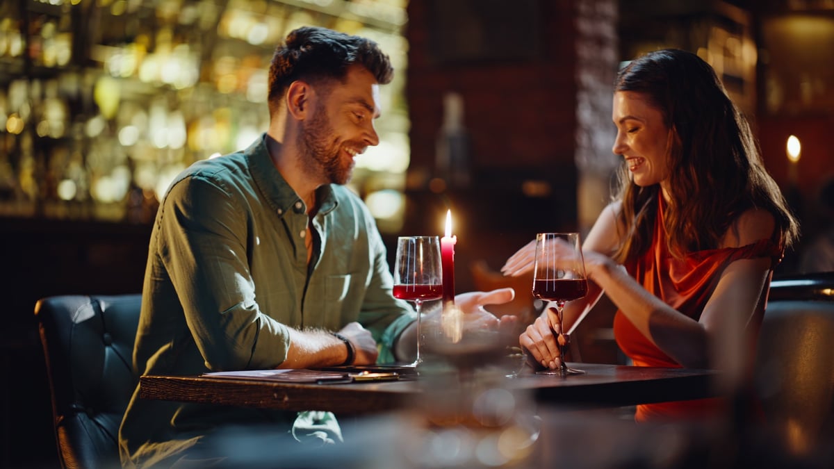Affectionate man taking woman hand confessing in love at cozy restaurant with wine glasses