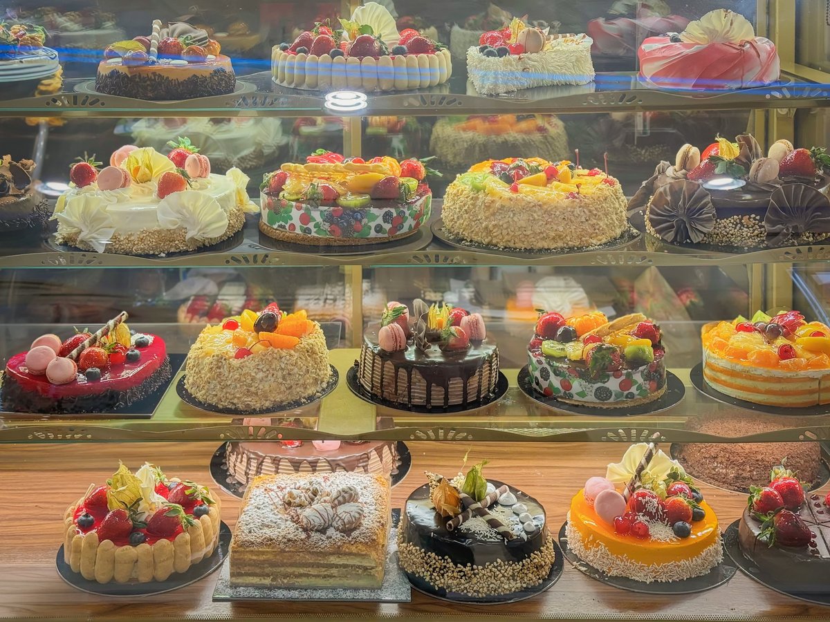 Large assortment of cakes displayed in bakery showcase with fruit topping chocolate glaze, cream decoration inside pastry shop