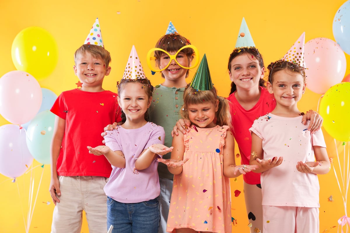 Happy kids in party hats under falling confetti on orange background