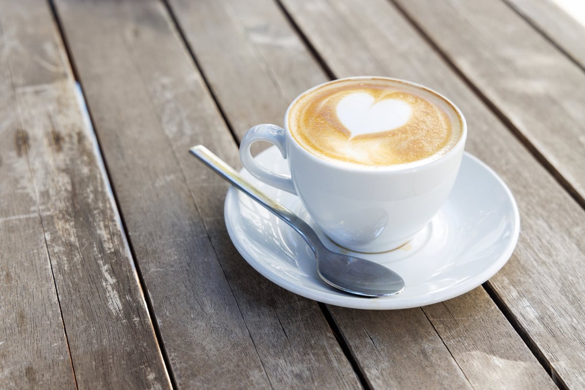 Cappuccino with heart latte art on a wooden table outdoors in sunny daylight, cozy cafe atmosphere