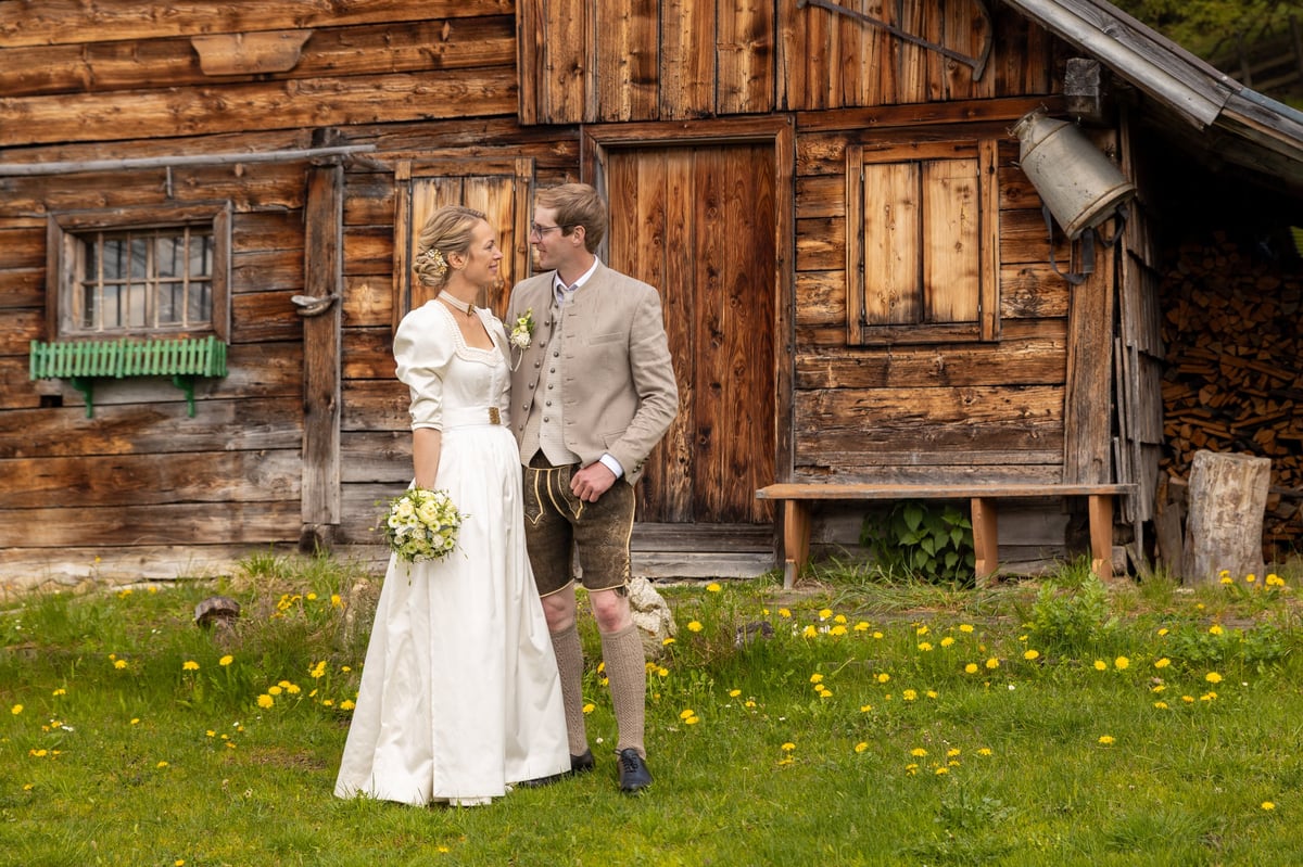 A couple in wedding attire stands close together in front of a rustic wooden cabin
