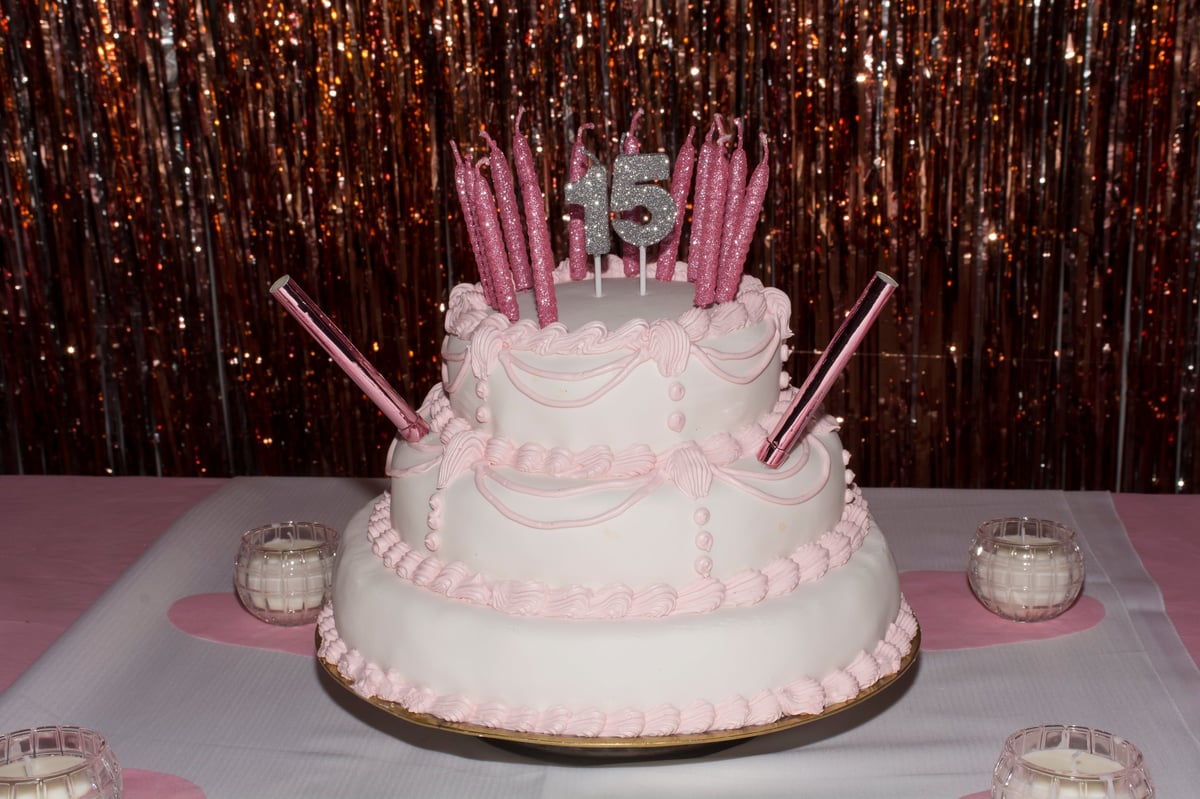 Pink and white cake with pink 15th birthday candles with the number 15 in silver